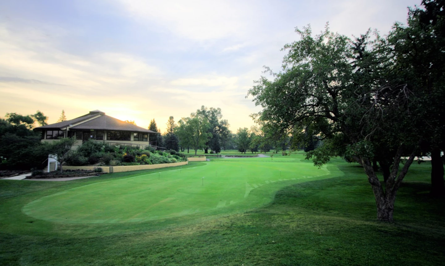Flatirons Golf Course clubhouse at golden hour with lush green putting green in the foreground