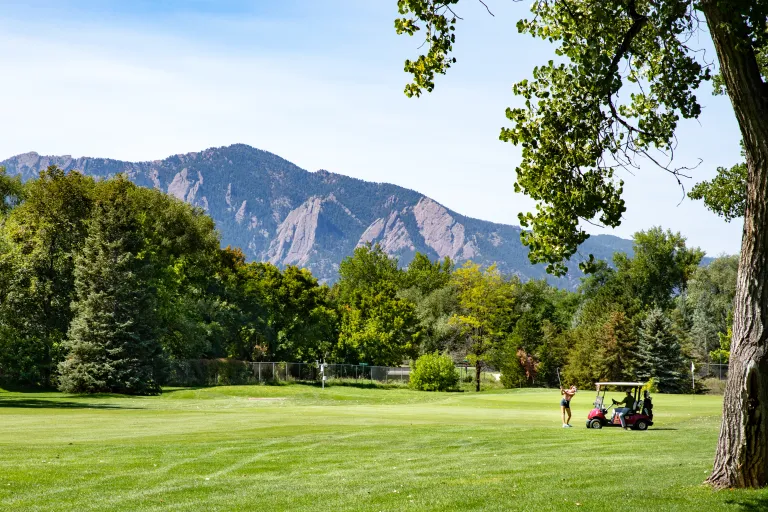 Golfer and cart on the fairway with the Flatirons rising dramatically behind