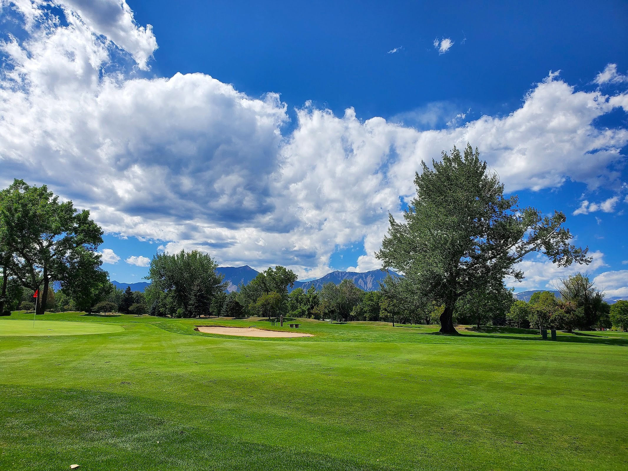 Well-maintained green and fairway with sand bunker under dramatic cloudy sky