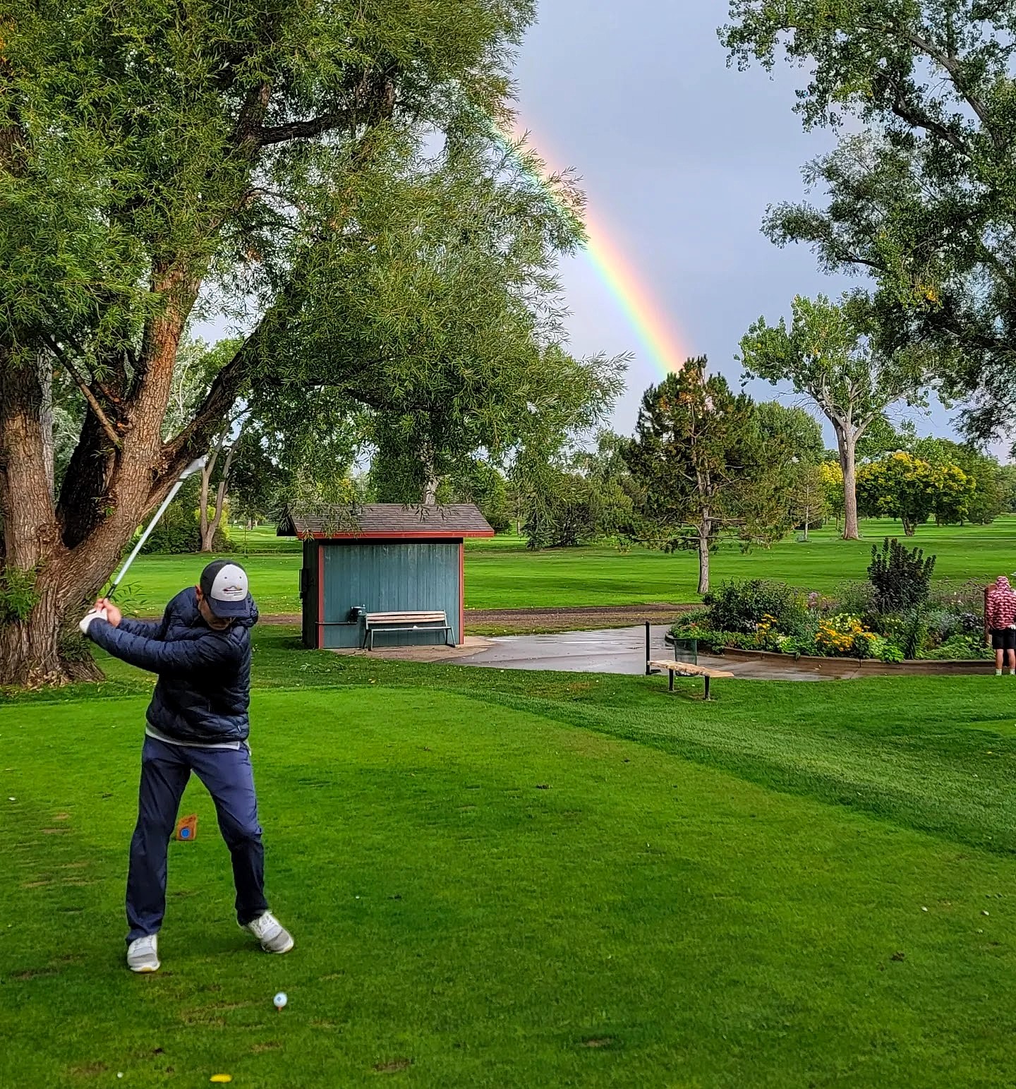 Golfer mid-swing with a rainbow arcing through the stormy Boulder sky
