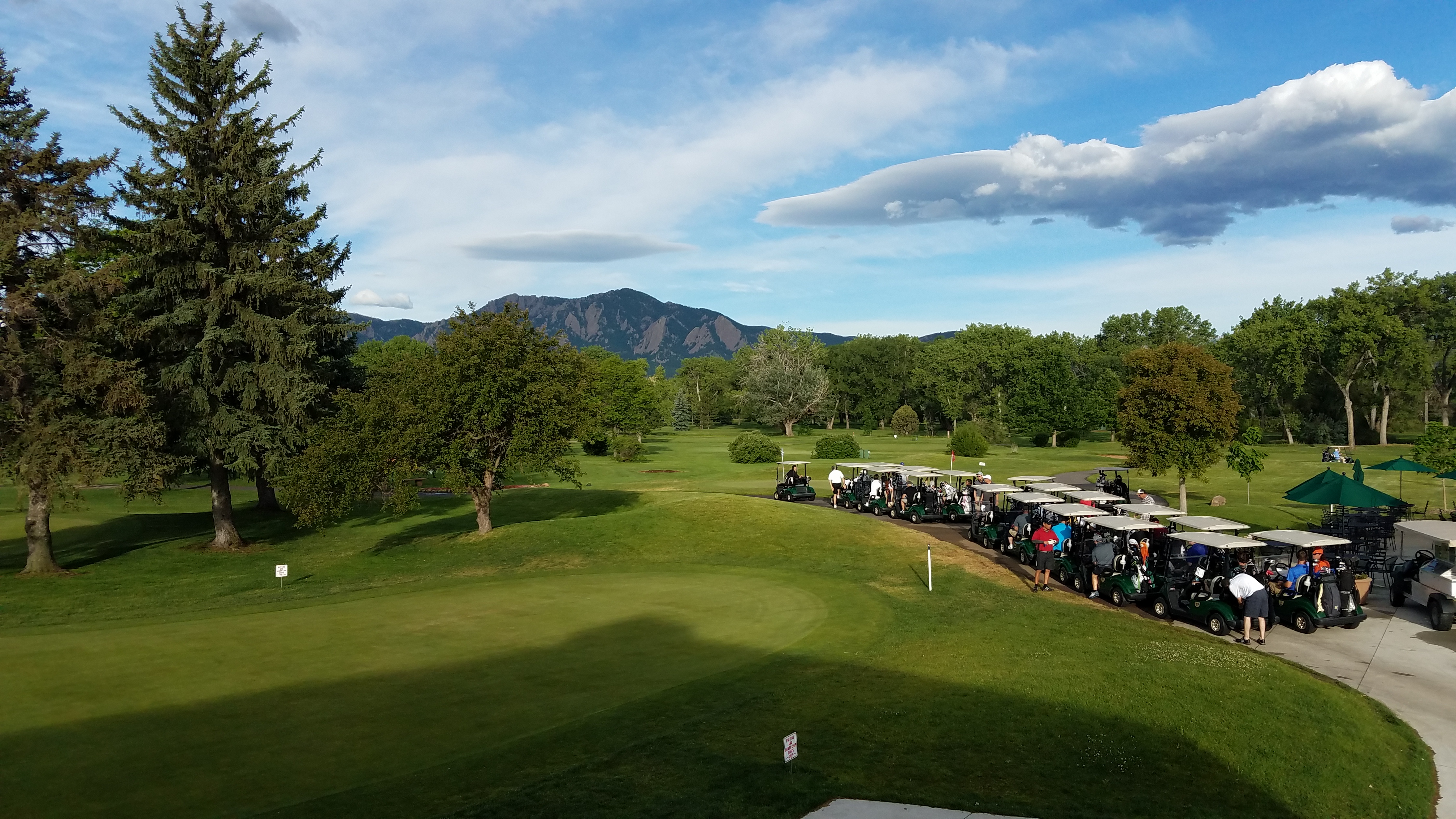Golf carts lined up with the Flatirons mountains visible through the treeline